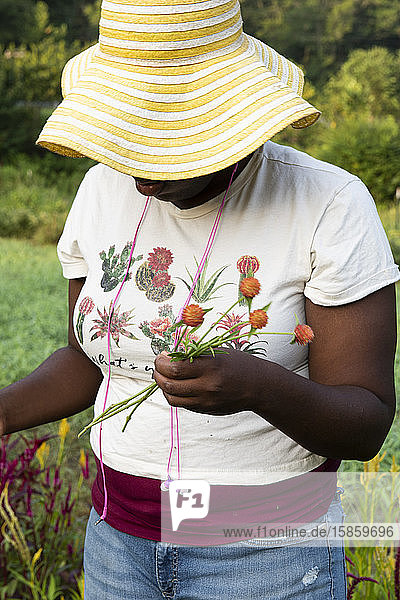 Schwarze Frau mit gelbem Sonnenhut und Ohrknöpfen schneidet Blumen auf dem Feld