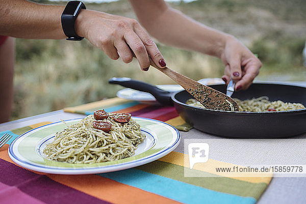 Nahaufnahme von Frauenhänden bei der Zubereitung von Pasta mit Pesto während einer Reise.