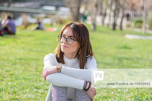Junges Mädchen  das im Gras eines Parks sitzt und nach rechts schaut