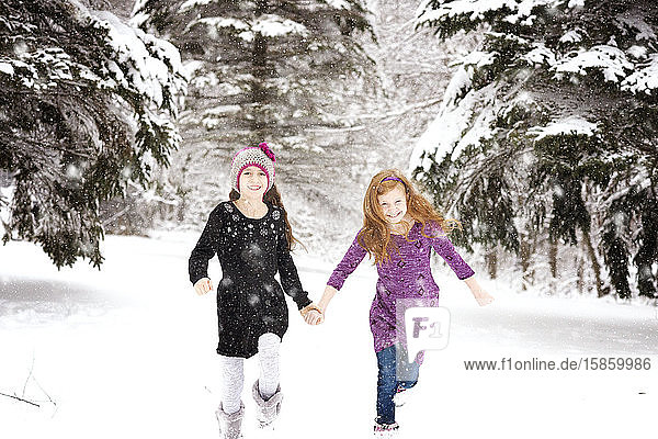 Two Young Girls Holding Hands Running Through Snowy Pine Trees