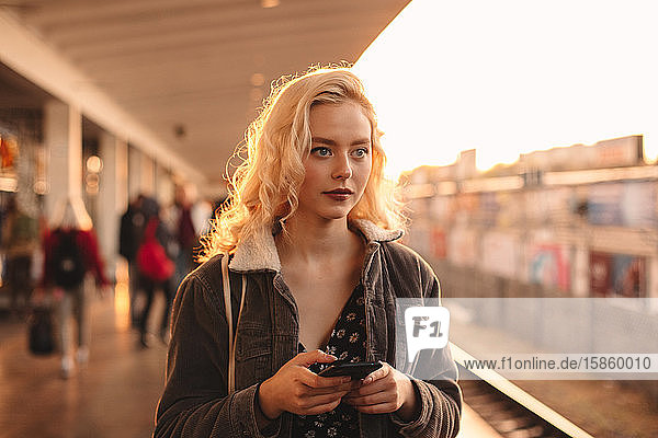 Young woman holding smart phone while waiting for train