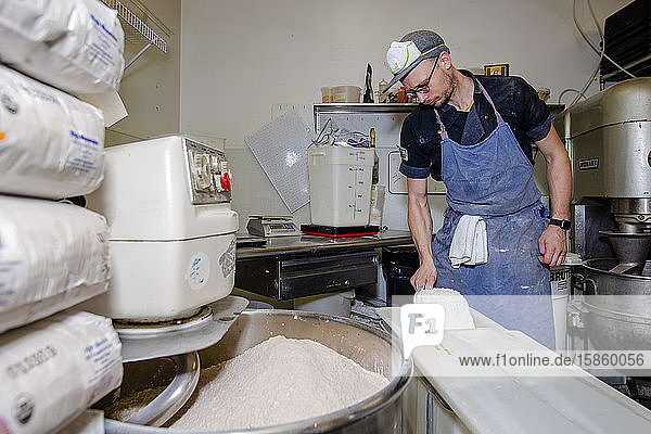 Ein professioneller Bäcker schöpft Brotmehl aus einem großen Plastikbehälter