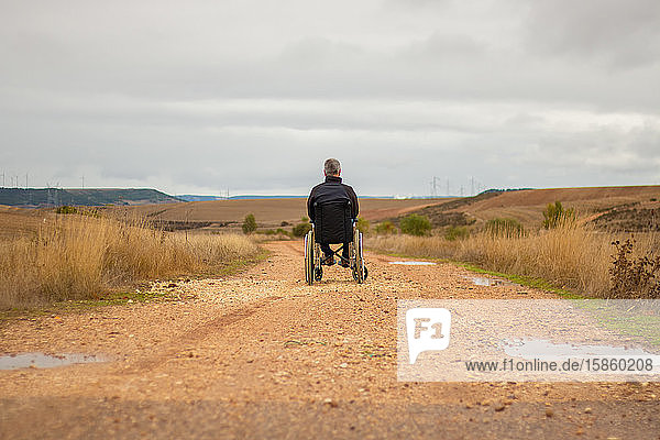 Rückansicht eines behinderten Mannes im Rollstuhl allein auf einem Weg