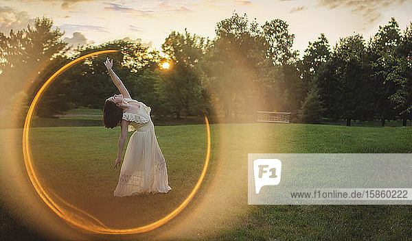 Eine Tänzerin steht in einem Lichtring und hebt bei Sonnenuntergang die Arme in den Himmel