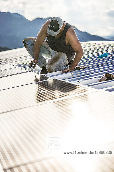 Arbeiter benutzt Handwerkzeug  um Sonnenkollektoren auf dem Dach des Gebäudes zu befestigen.