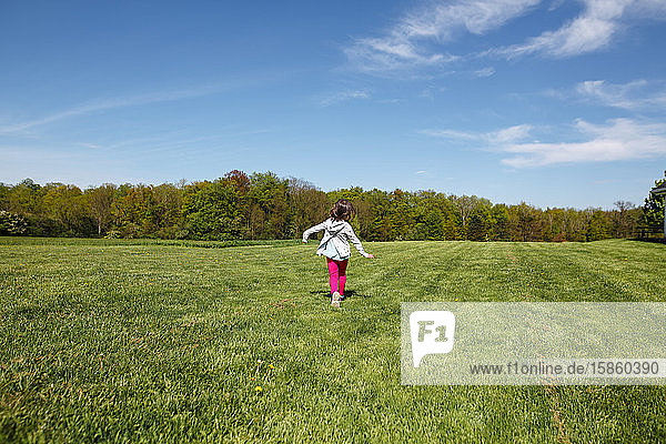 Ein fröhliches kleines Mädchen in heller Kleidung läuft im Frühling durch ein Feld