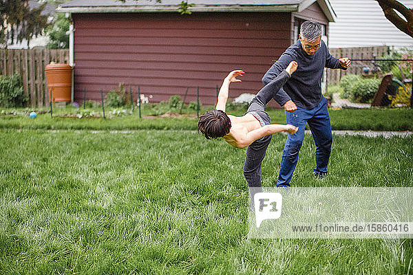 Ein Junge ohne Hemd rauft sich im Frühling mit seinem Vater auf dem Hof