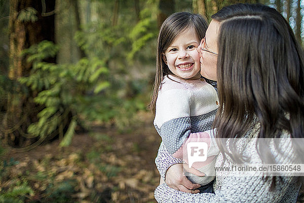 Mutter küsst im Wald ihre schöne süße Tochter auf die Wange.