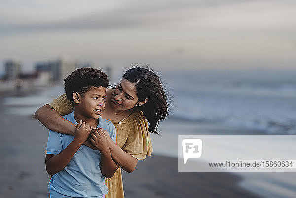 Nahaufnahme einer Mutter  die einen Jungen im Schulalter am Strand umarmt