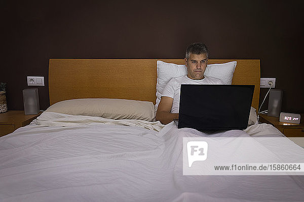 Mann arbeitet nachts an seinem Laptop im Bett