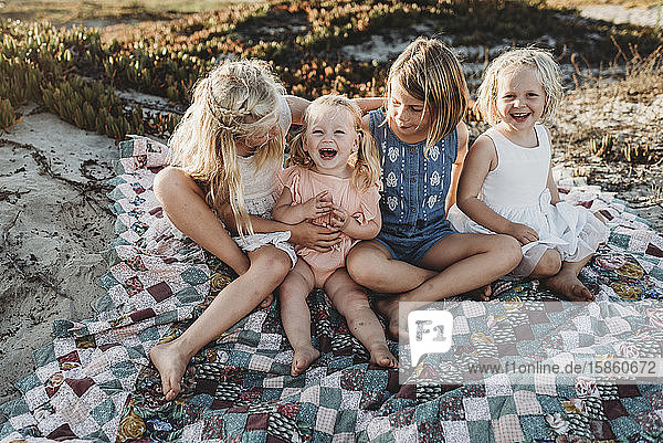 Vier Schwestern sitzen auf einer Decke am Strand und lachen über den Sonnenuntergang