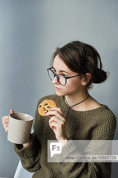 tausendjähriges braunhaariges Mädchen in Gläsern  das allein Tee mit Kuchen trinkt