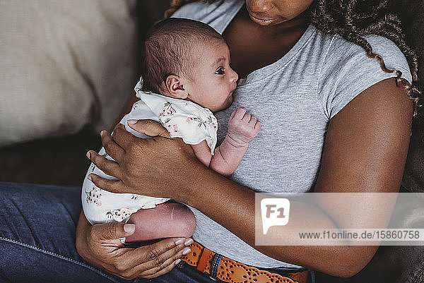 Schwarze Mutter in blauem Hemd hält mehrrassiges Neugeborenes