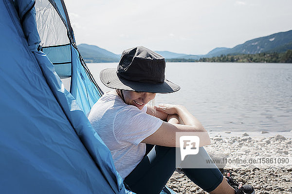 woman sitting in a tent smiling with sun hat on whilst camping