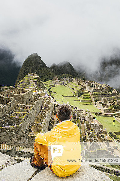 A man in a yellow jacket is sitting near ruins of Machu Picchu Peru
