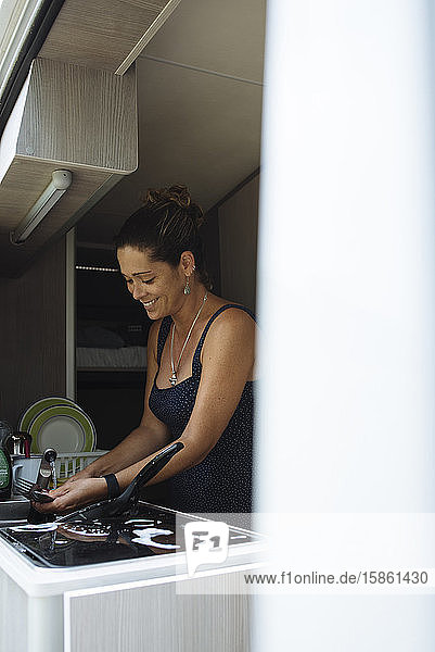 Frau mit Brötchen beim Geschirrspülen im Wohnmobil während eines Urlaubs.
