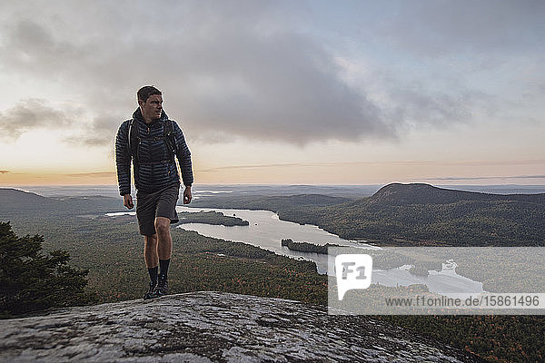 male hiker walks along Appalachian Trail with view at sunrise in Maine