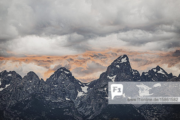 Setting sun reflects off clouds behind summits of the Tetons  Wyoming.