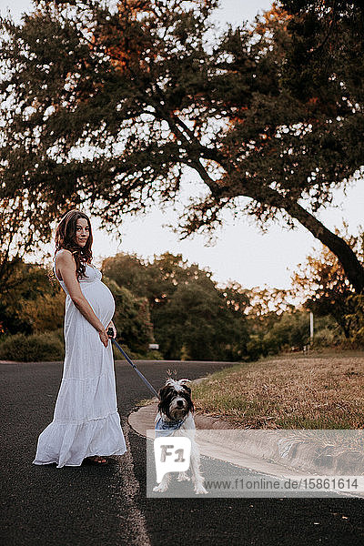 Schwangere Frau weißes Kleid beim Gassigehen mit ihrem Hund