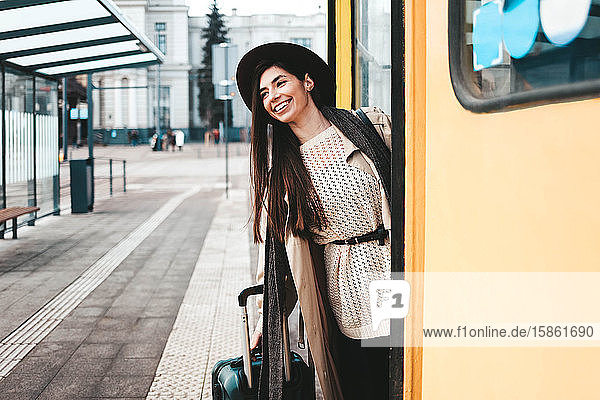 Hübsches Touristinnenmädchen in Mantel und Hut schaut aus einer Straßenbahntür