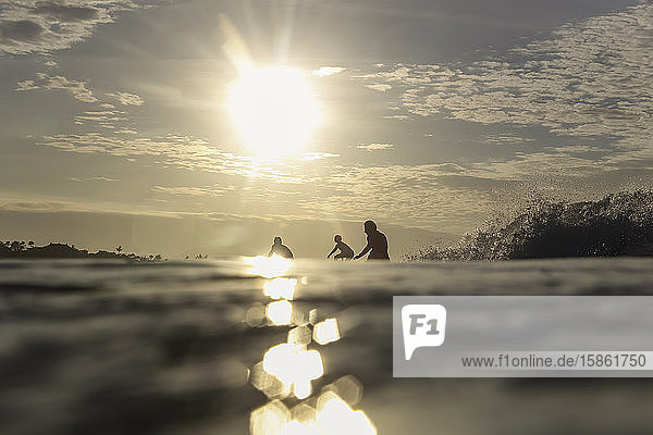 Drei Surfer bei Sonnenuntergang
