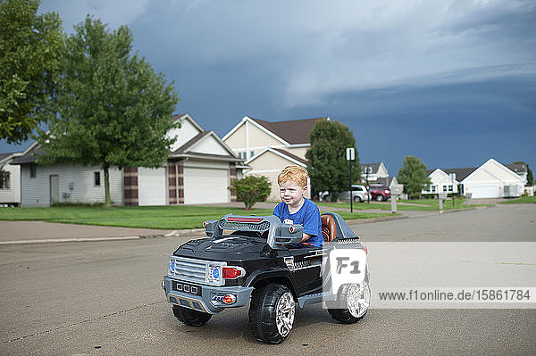 Junge fährt elektrisches Spielzeugauto in der Nachbarschaft