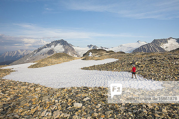 Wanderer überquert Schneefeld in felsigem Gelände.