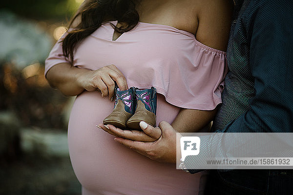 Couple holding baby boots in front of baby bump