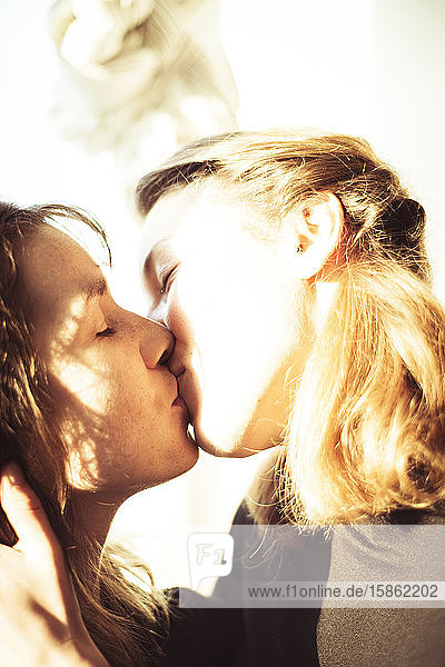 feminine lesbian couple kiss smiling in warm sunshine in window