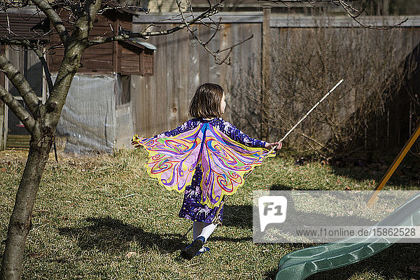 A happy child runs through a garden in Spring wearing butterfly wings