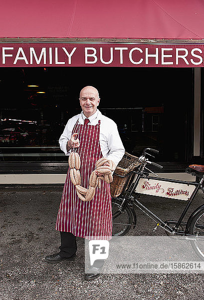 Butcher holding sausage in front of his shop