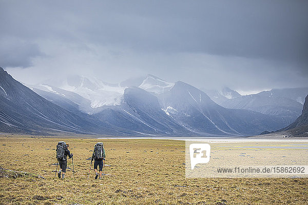 Rückansicht von zwei Rucksacktouristen  die durch ein offenes Tal in der Arktis wandern.