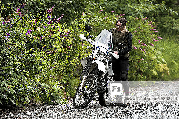 A women takes a break from motorcycle riding and stands with her bike.