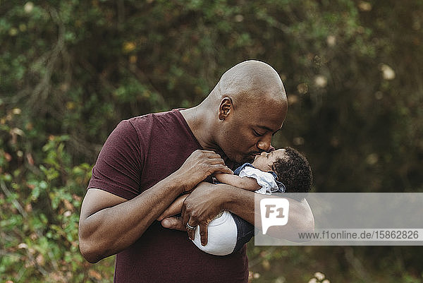 Close up happy father holding and kissing newborn girl outside