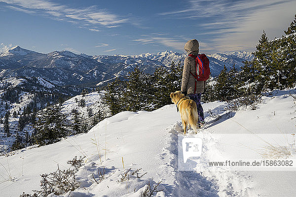 Wanderin und Hund blicken in der verschneiten Berglandschaft in die Ferne