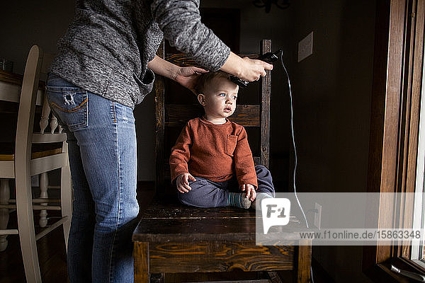 Junge wird zu Hause von seiner Mutter auf einem Stuhl frisiert