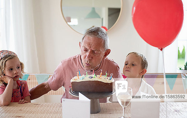 Opa saß mit seinen Enkelkindern an seinem Geburtstag und blies Kerzen aus