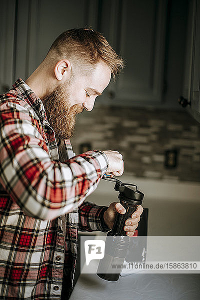 Mann mit Bart lächelt morgens beim Kaffeemahlen in seiner Küche