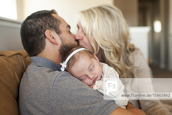 Close up of newborn baby sleeping with parents kissing in background