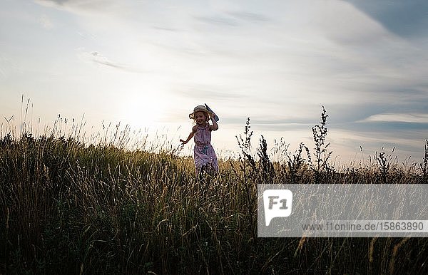 Mädchen rennt bei Sonnenuntergang mit einem Papierflugzeug über eine Wiese