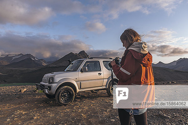 Junge Frau schaut in den Bergen vor dem Auto in die Kamera