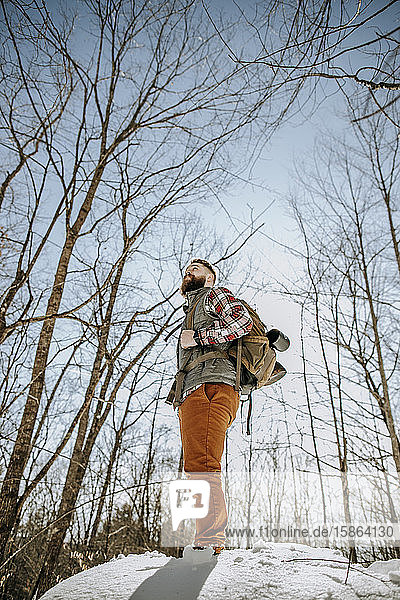Mann mit Bart schaut beim Wandern in verschneiten Wäldern in die Ferne