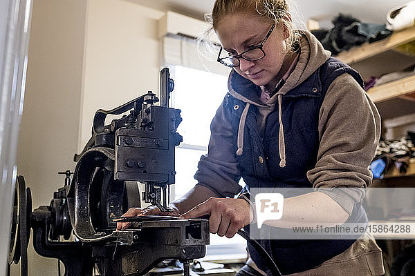 Female saddler standing in workshop  sewing leather strap on saddlery sewing machine.