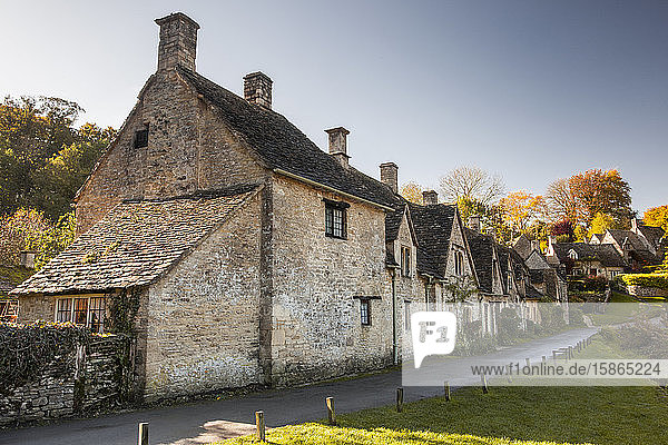 The midday sun casts its light across a row of medieval houses at Arlington Row  Bibury in Gloucestershire  Cotswolds  England  United Kingdom  Europe