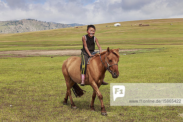 Pferd und lächelnder Junge reiten ohne Sattel mit Ger und Hügeln dahinter im Sommernomadenlager  Khujirt  Uvurkhangai (Ovorkhangai)  Zentralmongolei  Zentralasien  Asien