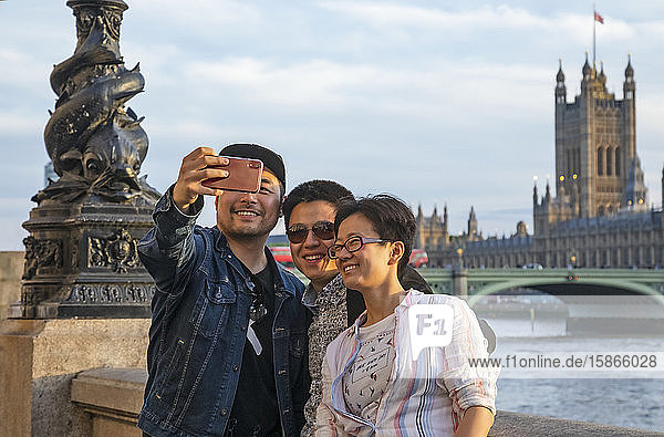 Touristen machen ein Selbstporträt entlang der Themse mit dem Victoria Tower und der London Bridge im Hintergrund; London  England