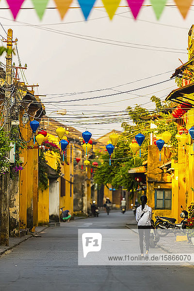 Fußgänger auf einer Straße mit gelben Gebäuden und bunten Laternen  die über der Straße aufgereiht sind; Hoi An  Provinz Quang Nam  Vietnam