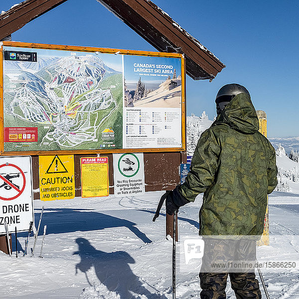 Downhill skiier looking at information board and map at Sun Peaks Resort; Sun Peaks British Columbia Canada