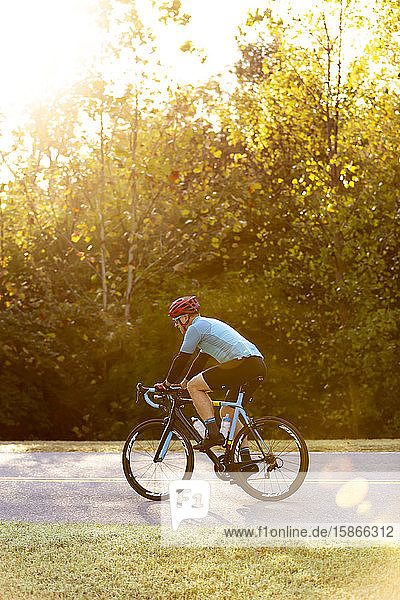 Cyclist riding on a road with bright sunlight filtering through the trees  near Trace Nachez Bridge; Franklin  Tennessee  United States of America