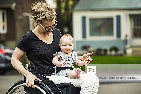 Eine querschnittsgelähmte Mutter  die ihr Baby auf dem Schoß trägt  während sie einen Rollstuhl benutzt  an einem warmen Sommernachmittag im Freien: Edmonton  Alberta  Kanada